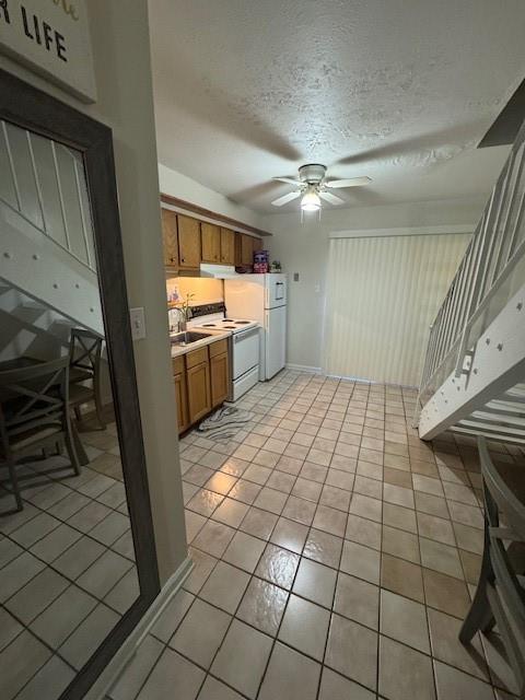 kitchen with brown cabinets, a textured ceiling, white appliances, light countertops, and ceiling fan