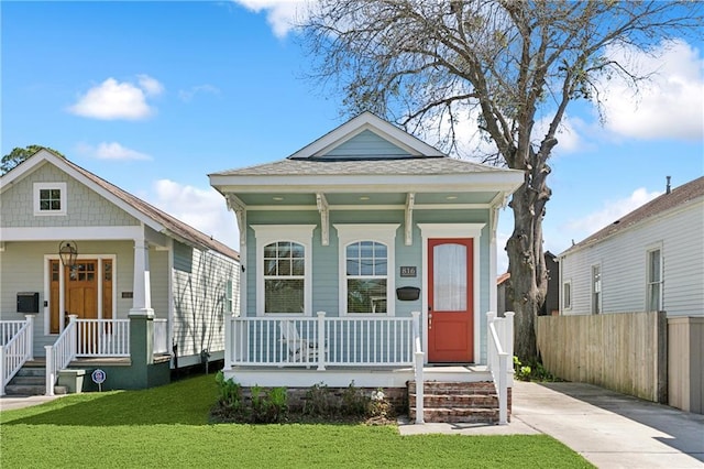 shotgun-style home featuring covered porch, a front yard, and fence