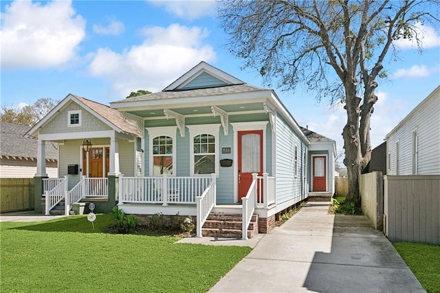 shotgun-style home featuring a front lawn, fence, covered porch, and a shingled roof