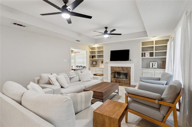 living area featuring built in features, ceiling fan, visible vents, light tile patterned flooring, and a raised ceiling
