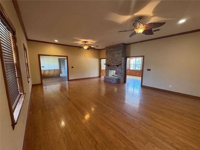 unfurnished living room featuring a ceiling fan, wood finished floors, a multi sided fireplace, crown molding, and baseboards