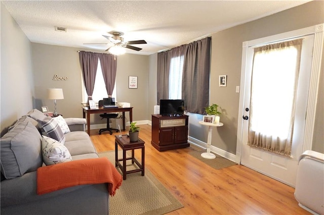 living area with light wood finished floors, visible vents, baseboards, ceiling fan, and a textured ceiling