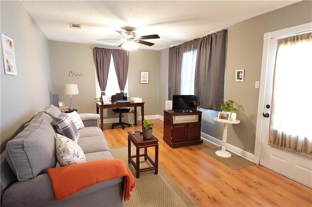 living area with baseboards, visible vents, ceiling fan, a textured ceiling, and light wood-type flooring