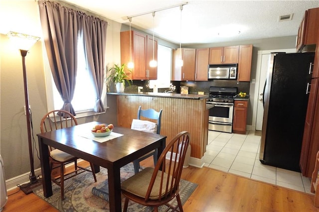 kitchen with a peninsula, decorative backsplash, light wood-style floors, appliances with stainless steel finishes, and dark countertops