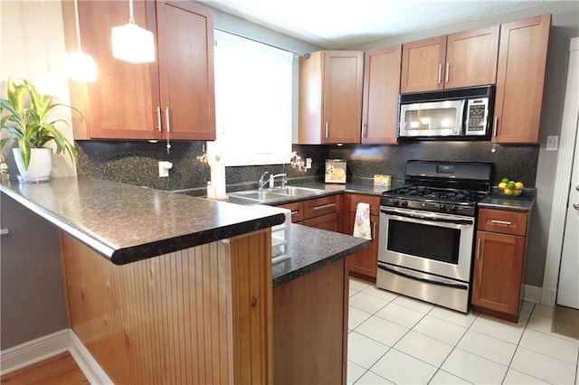 kitchen featuring dark countertops, tasteful backsplash, a peninsula, stainless steel appliances, and a sink