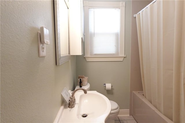 bathroom featuring tile patterned flooring, baseboards, toilet, shower / bath combo, and a sink