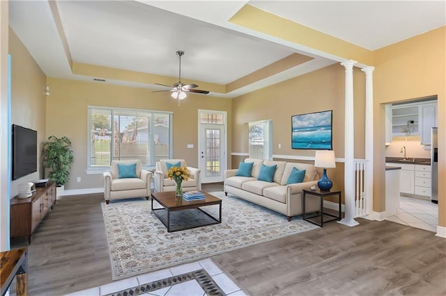 living area with a tray ceiling, baseboards, wood finished floors, and decorative columns