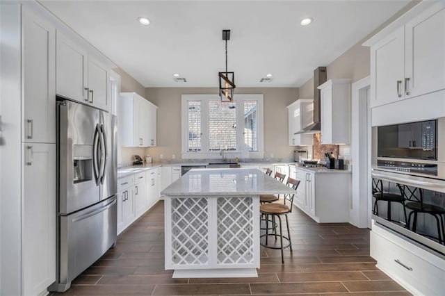 926 City Park Ave, New Orleans, LA 70119 - kitchen featuring wood finish floors, a kitchen bar, appliances with stainless steel finishes, white cabinets, and wall chimney range hood