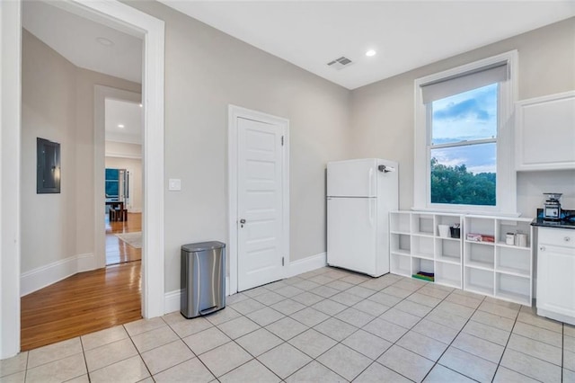 926 City Park Ave, New Orleans, LA 70119 - kitchen with visible vents, electric panel, white cabinetry, freestanding refrigerator, and light tile patterned floors