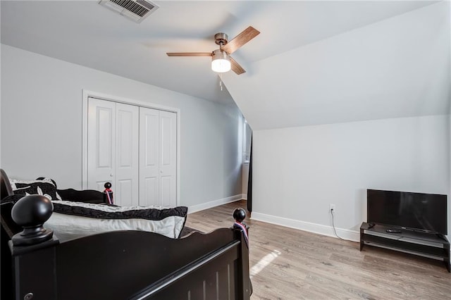 bedroom with light wood-type flooring, visible vents, lofted ceiling, a closet, and baseboards