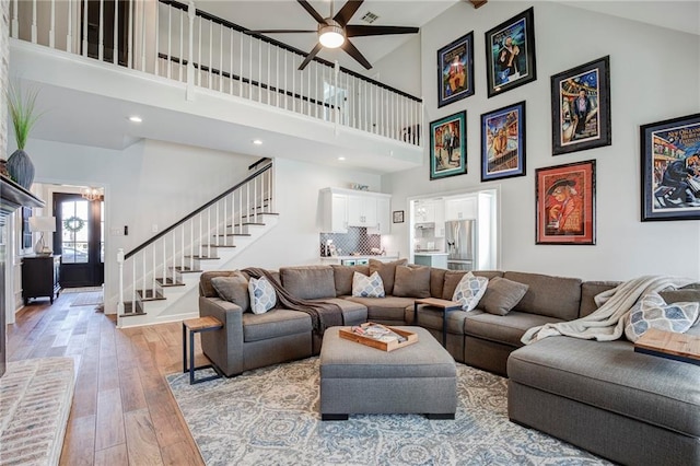 living room featuring a ceiling fan, a high ceiling, light wood-style flooring, and stairs