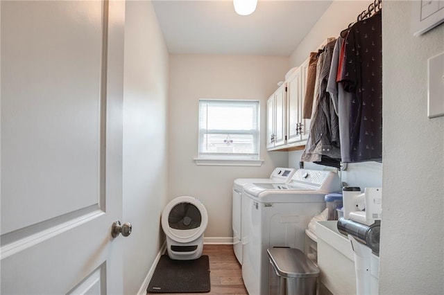 clothes washing area featuring light wood-type flooring, cabinet space, baseboards, and washing machine and clothes dryer