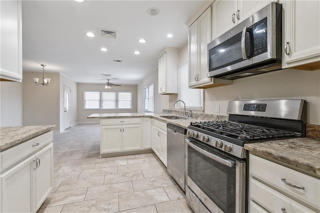 kitchen with light stone counters, a peninsula, a sink, appliances with stainless steel finishes, and ceiling fan with notable chandelier