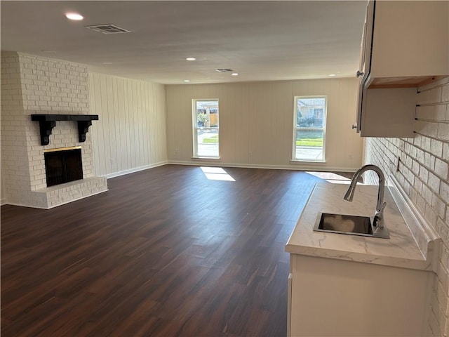 unfurnished living room with visible vents, a sink, dark wood-style floors, a fireplace, and baseboards