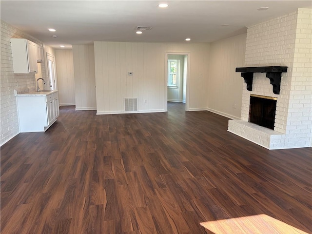 unfurnished living room featuring a sink, visible vents, dark wood-style floors, and a fireplace