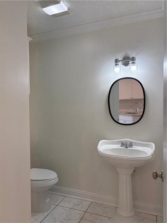 half bathroom with baseboards, toilet, marble finish floor, and a textured ceiling