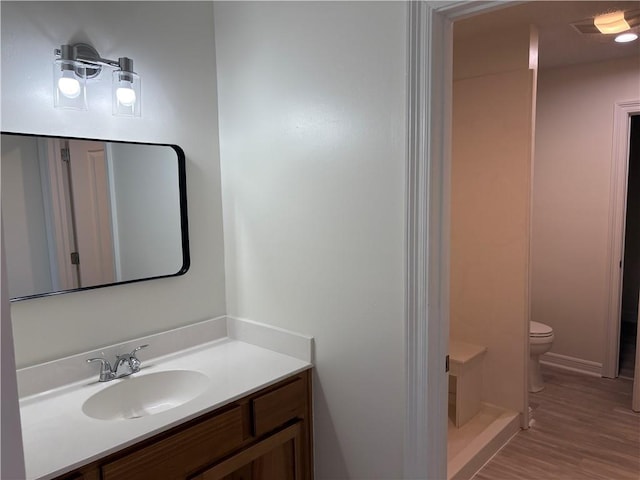 bathroom with toilet, vanity, walk in shower, and wood finished floors