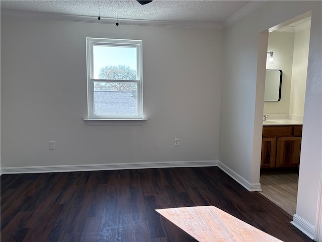 empty room with dark wood finished floors, a textured ceiling, baseboards, and a sink