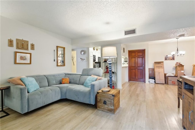 living room with an inviting chandelier, light wood-style flooring, visible vents, and a textured ceiling