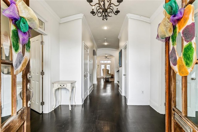 hallway with ornamental molding, arched walkways, an inviting chandelier, baseboards, and dark wood-style flooring