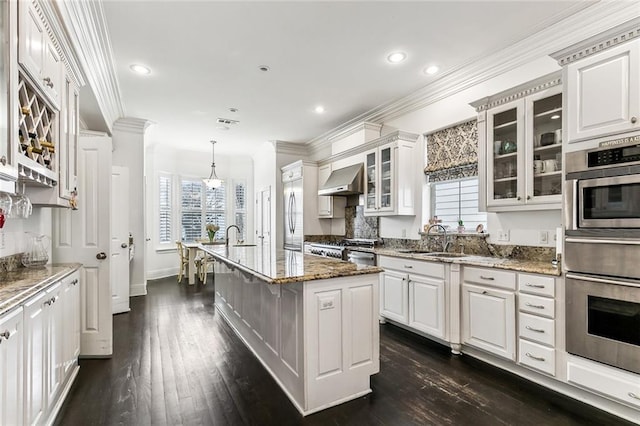 kitchen with dark wood finished floors, stainless steel appliances, a sink, white cabinets, and wall chimney exhaust hood