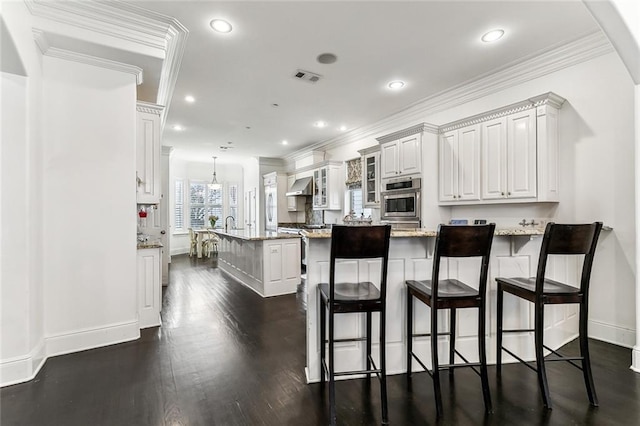 kitchen with visible vents, glass insert cabinets, wall chimney range hood, a peninsula, and dark wood-style flooring