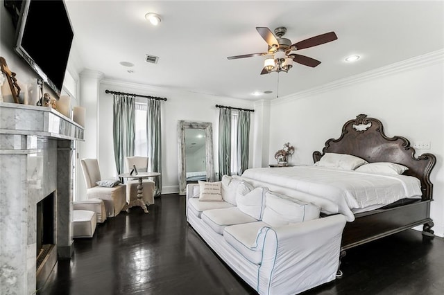 bedroom with visible vents, ornamental molding, wood finished floors, a fireplace, and ceiling fan