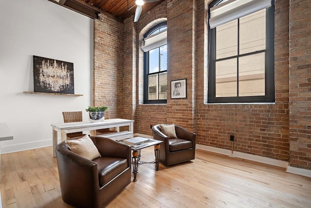 living area with beamed ceiling, wood finished floors, brick wall, baseboards, and a towering ceiling