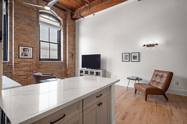 office space with baseboards, brick wall, light wood-style flooring, wooden ceiling, and beamed ceiling