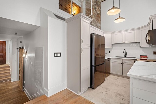 kitchen featuring light stone counters, dishwashing machine, freestanding refrigerator, a towering ceiling, and a sink