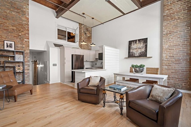 living area featuring beam ceiling, brick wall, a high ceiling, and light wood-style floors