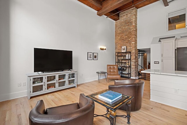 living area with beamed ceiling, baseboards, a high ceiling, and light wood finished floors