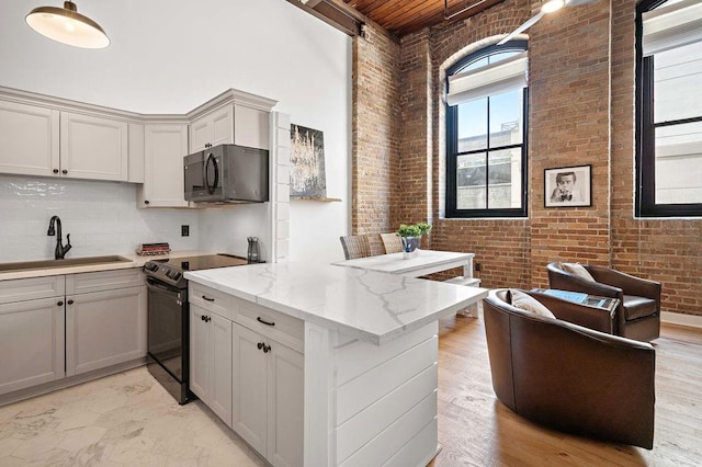 kitchen with black appliances, a sink, a peninsula, brick wall, and a towering ceiling