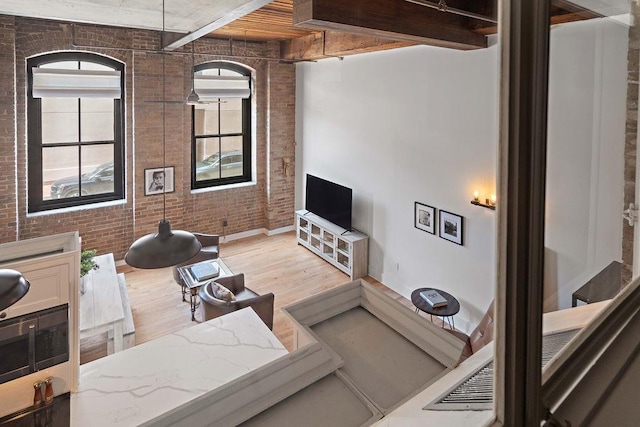 living room featuring light wood-style flooring, baseboards, beamed ceiling, and brick wall