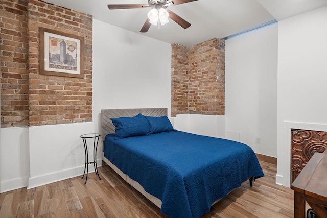 bedroom with a ceiling fan, wood finished floors, and brick wall