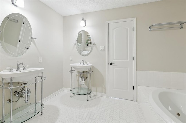 bathroom featuring baseboards, a sink, a textured ceiling, tile patterned floors, and a bath