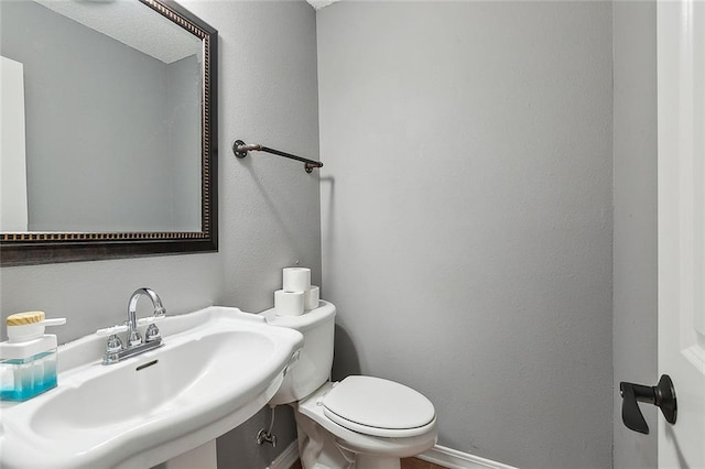 bathroom featuring toilet, baseboards, and a sink