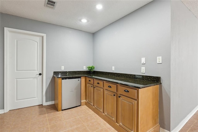 interior space featuring visible vents, fridge, dark stone counters, light tile patterned flooring, and brown cabinetry