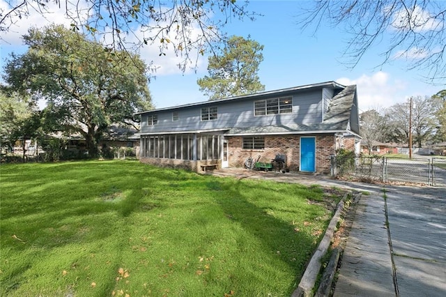 back of house with brick siding, a lawn, fence, and a sunroom