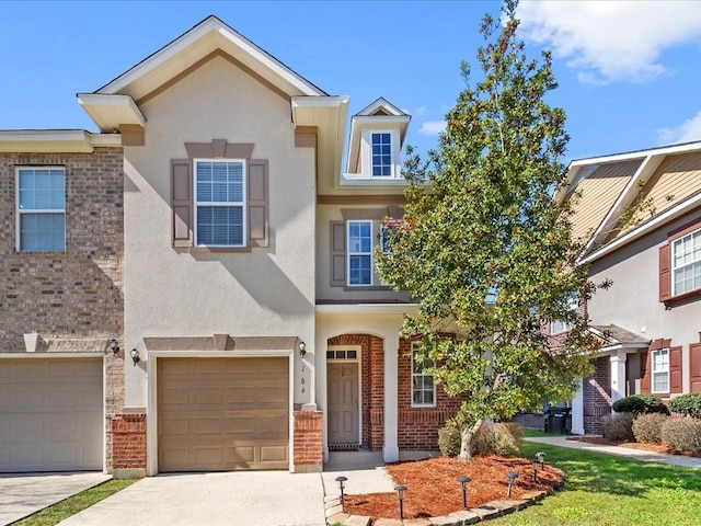 view of front of property featuring stucco siding, driveway, brick siding, and an attached garage