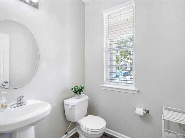 bathroom with toilet, wood finished floors, baseboards, and a sink