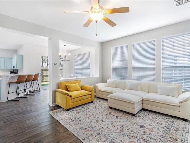 living room featuring ceiling fan with notable chandelier, dark wood-style floors, visible vents, and baseboards