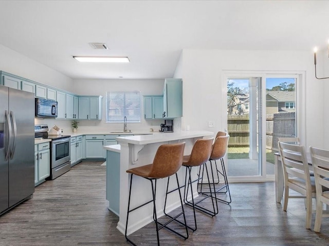 kitchen featuring a sink, a kitchen breakfast bar, appliances with stainless steel finishes, a peninsula, and light countertops