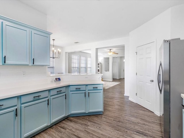 kitchen featuring blue cabinetry, dark wood-style floors, freestanding refrigerator, a peninsula, and decorative backsplash