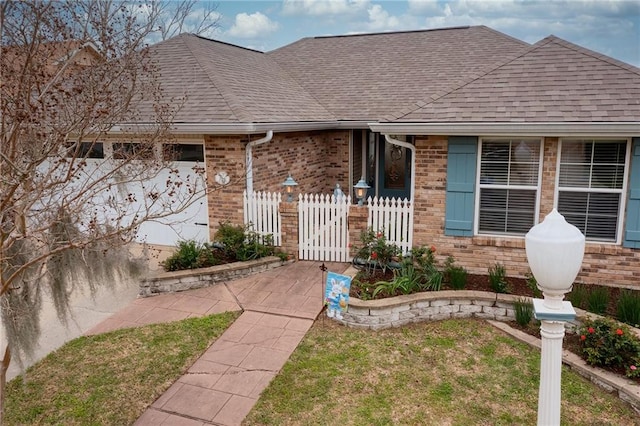 view of front facade featuring a front yard, a gate, fence, a shingled roof, and brick siding