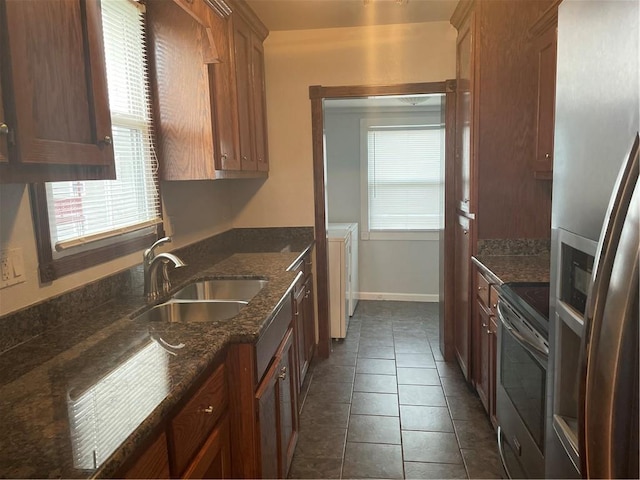 kitchen with dark stone countertops, baseboards, dark tile patterned flooring, a sink, and stainless steel appliances