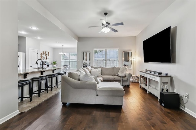 living area featuring ceiling fan with notable chandelier, dark wood-type flooring, and baseboards