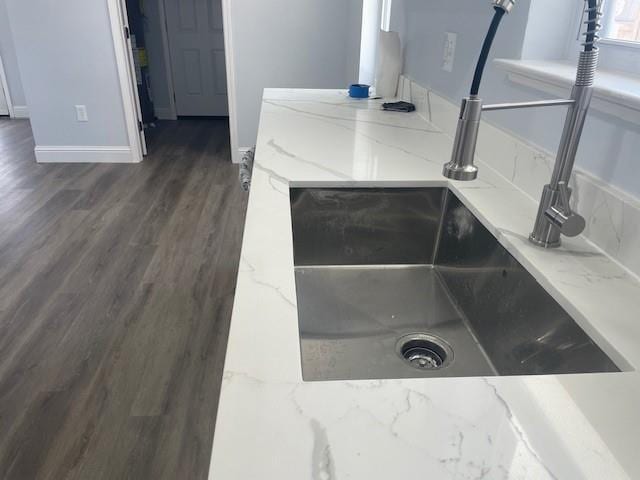 room details featuring light stone counters, baseboards, wood finished floors, and a sink