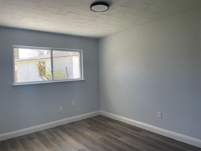 unfurnished room featuring dark wood-style floors and baseboards