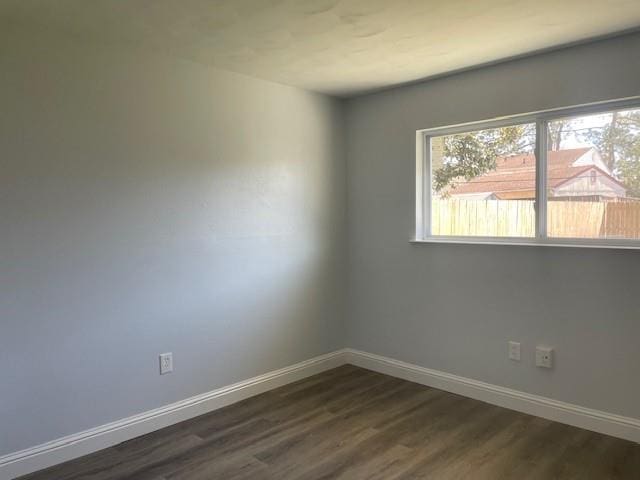 spare room with baseboards and dark wood-type flooring